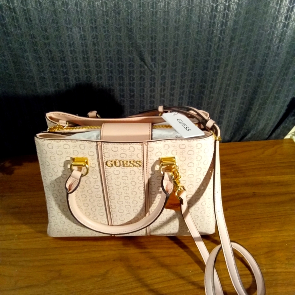 A rose colored Guess handbag  with a gold zipper in the middle and a flap cover.